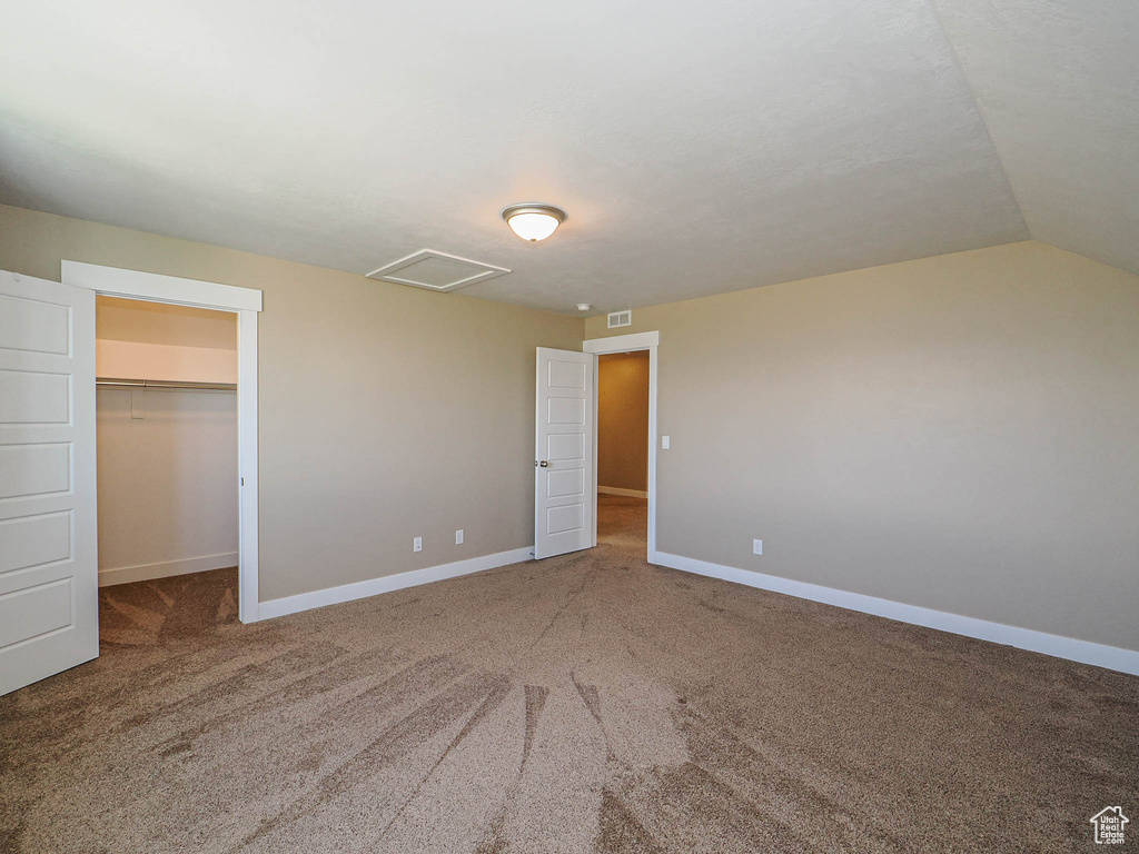 Unfurnished bedroom featuring carpet floors, a walk in closet, baseboards, a closet, and lofted ceiling