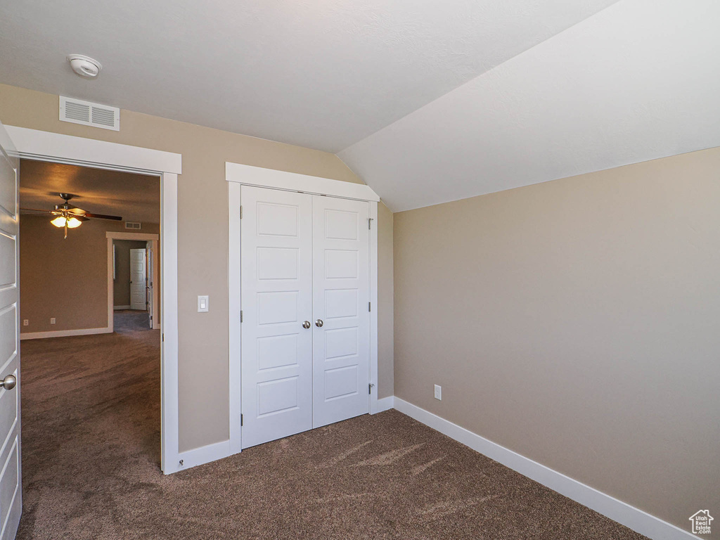 Unfurnished bedroom with dark colored carpet, baseboards, a closet, and vaulted ceiling