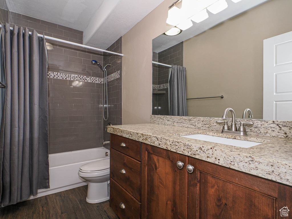 Full bathroom featuring wood finished floors, toilet, shower / bath combo with shower curtain, and vanity