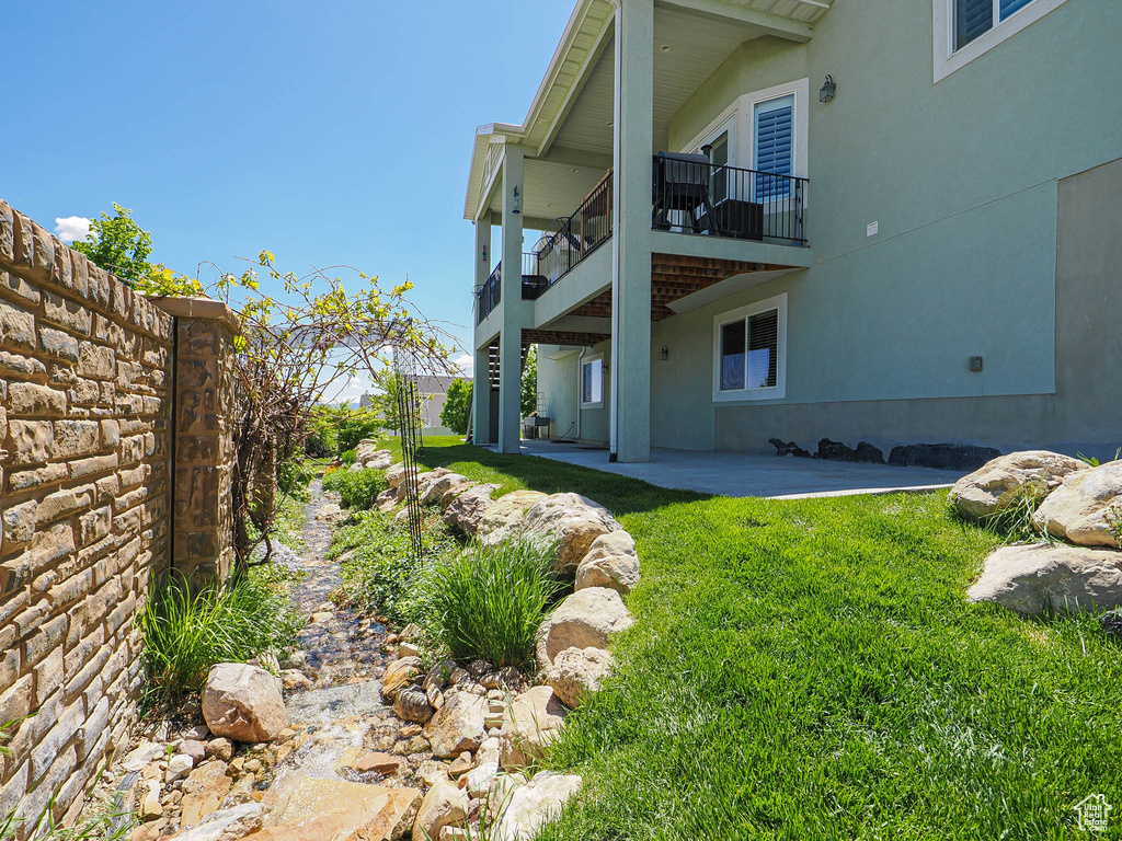 View of grassy yard featuring a patio area and a balcony