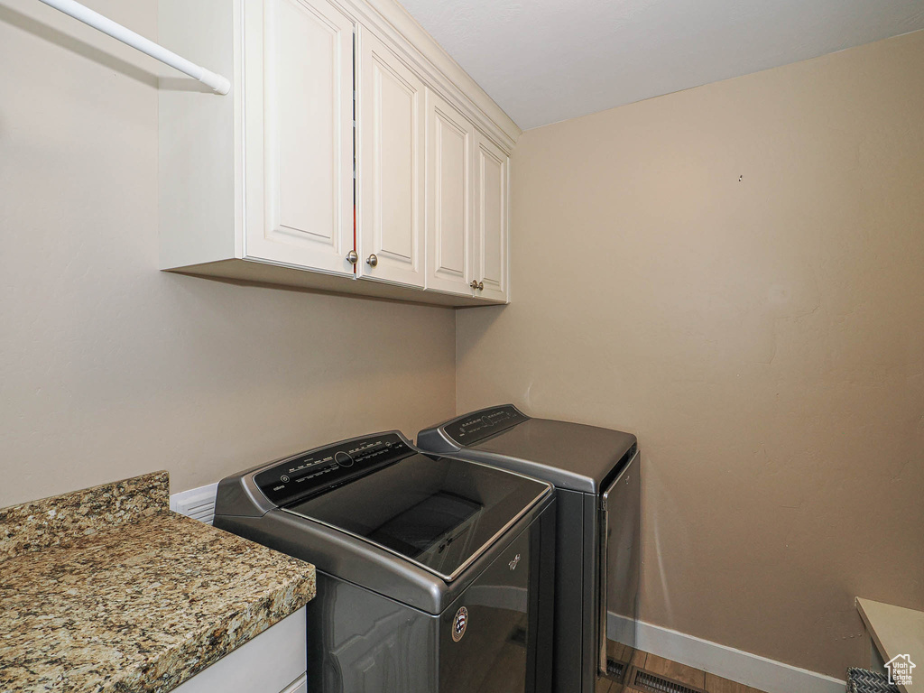 Clothes washing area featuring cabinet space, washer and dryer, baseboards, and dark wood-style floors