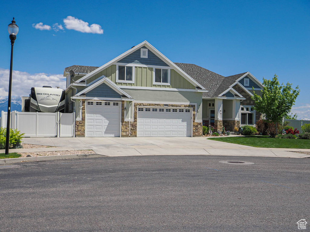 Craftsman-style home featuring fence, stone siding, an attached garage, board and batten siding, and concrete driveway