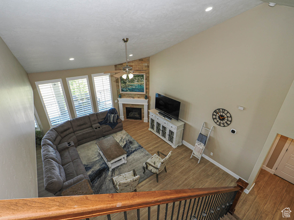 Living area featuring lofted ceiling, a ceiling fan, a large fireplace, wood finished floors, and baseboards