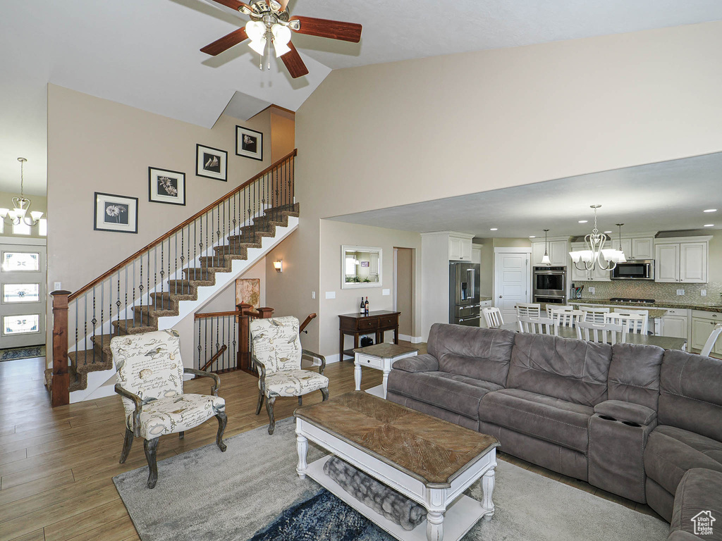 Living area with a chandelier, high vaulted ceiling, light wood-type flooring, stairway, and ceiling fan