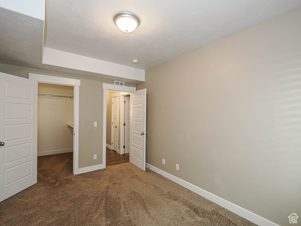 Unfurnished bedroom featuring baseboards, carpet floors, a walk in closet, and a closet