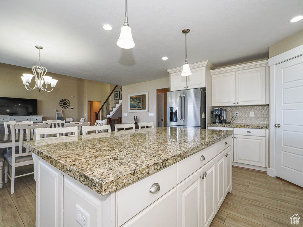 Kitchen with high end fridge, light wood-style floors, a center island, a chandelier, and decorative light fixtures