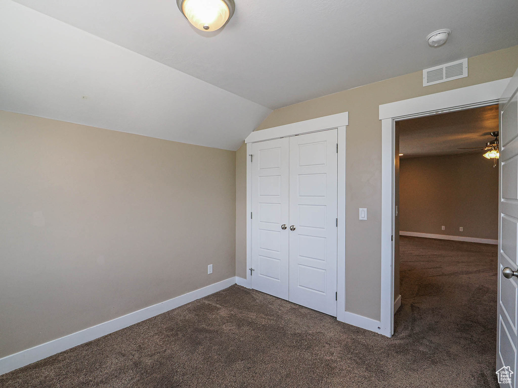 Unfurnished bedroom with dark colored carpet, baseboards, a closet, and lofted ceiling