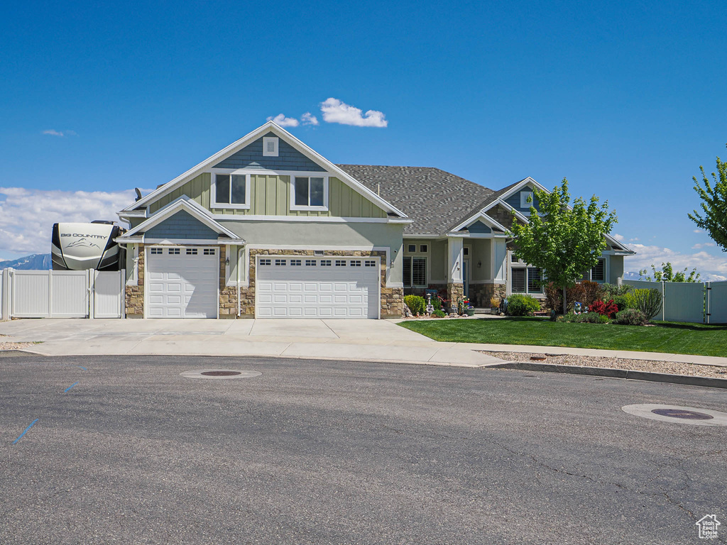 Craftsman house with stone siding, driveway, an attached garage, a gate, and board and batten siding
