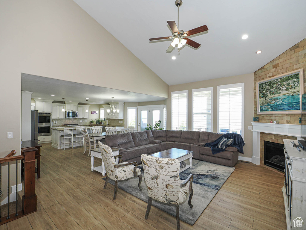 Living room with ceiling fan, high vaulted ceiling, a fireplace, light wood-style flooring, and a chandelier
