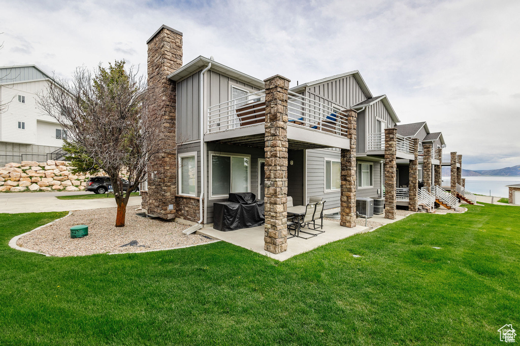 Back of property with board and batten siding, a balcony, a lawn, a patio area, and central air condition unit