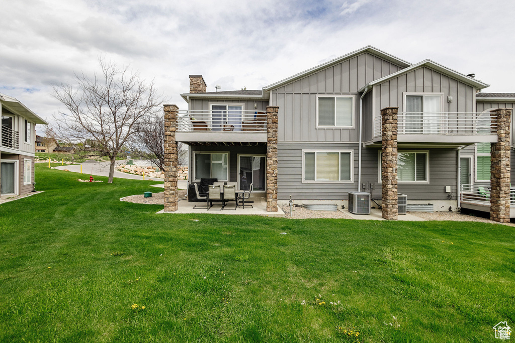 Back of property with a balcony, board and batten siding, a patio, a chimney, and a lawn