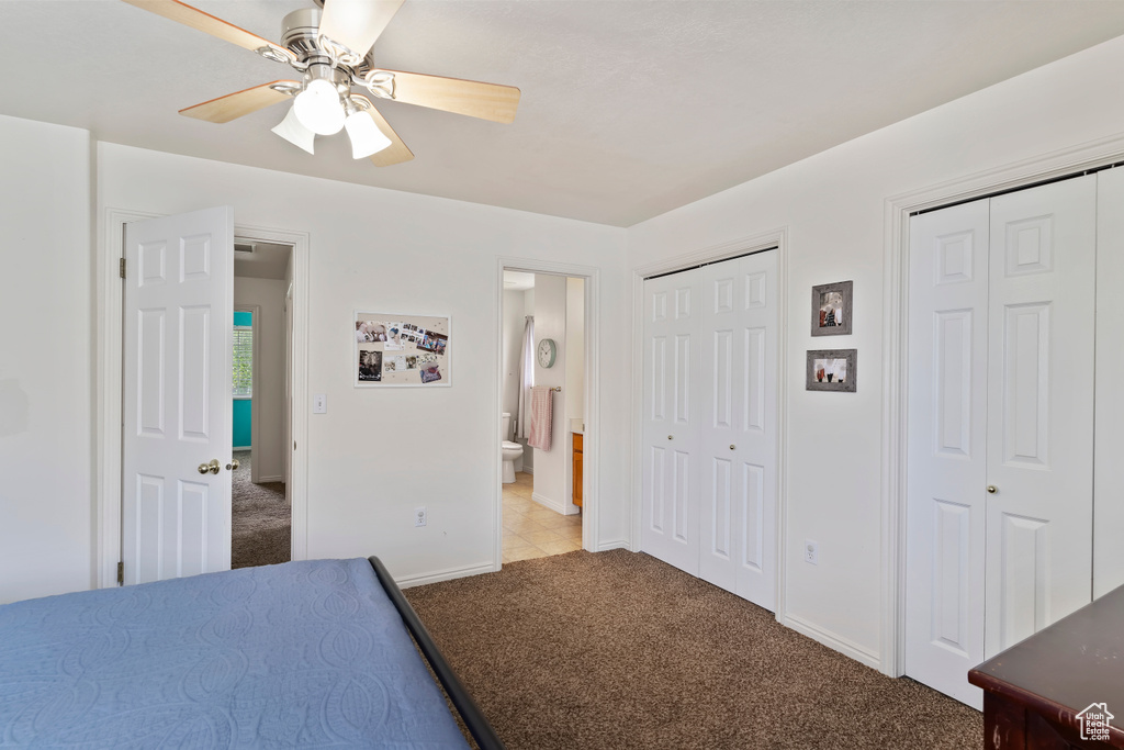 Carpeted bedroom with two closets, baseboards, connected bathroom, and a ceiling fan
