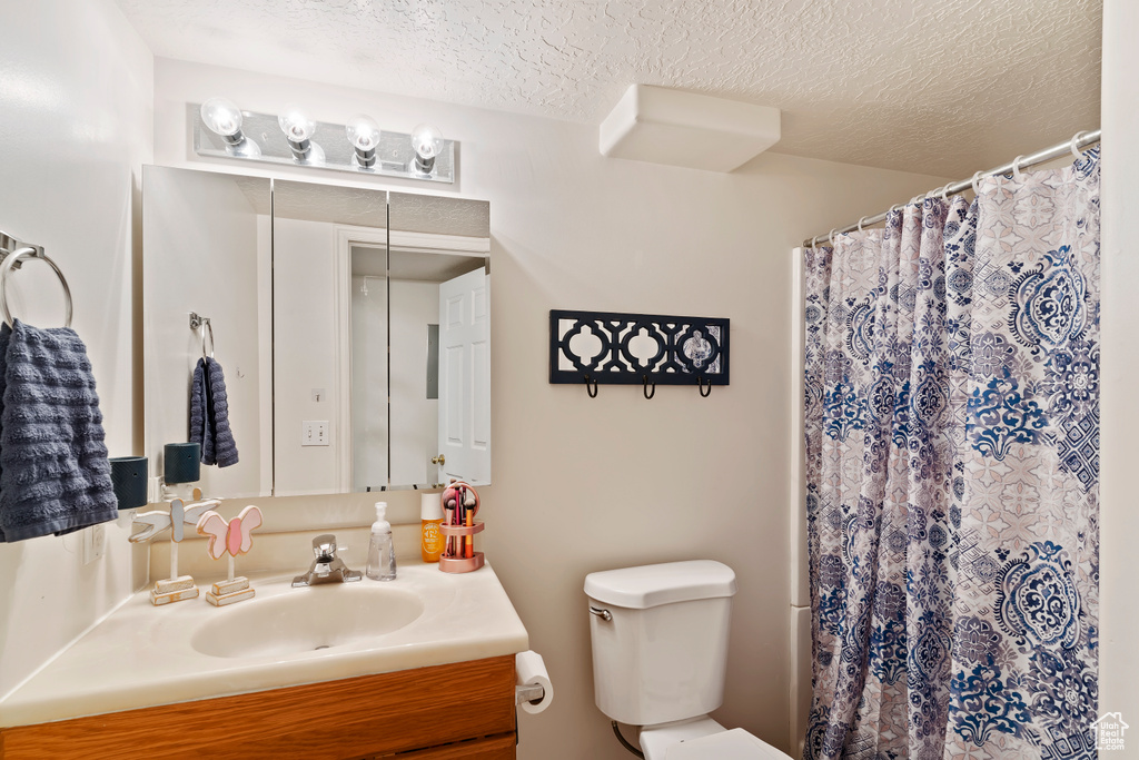 Bathroom featuring a textured ceiling, toilet, vanity, and curtained shower
