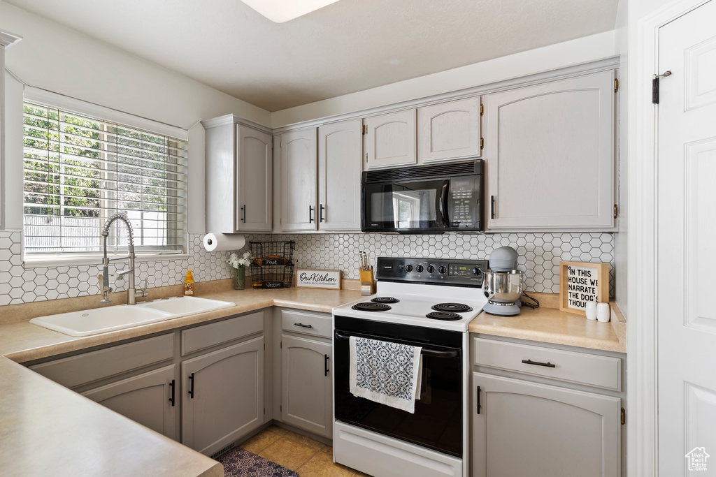 Kitchen with black microwave, range with electric stovetop, a sink, backsplash, and light countertops