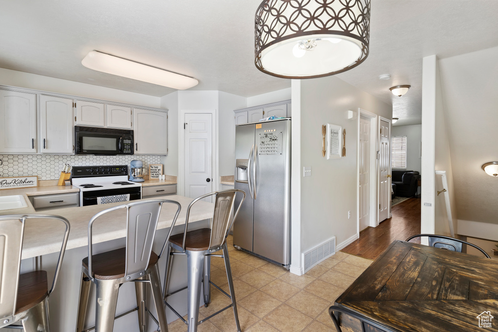 Kitchen featuring stainless steel refrigerator with ice dispenser, electric range, black microwave, a peninsula, and baseboards