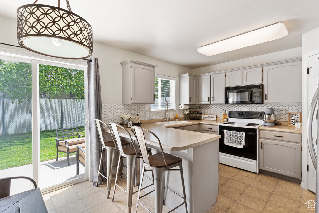 Kitchen with black microwave, electric stove, a sink, a peninsula, and decorative backsplash