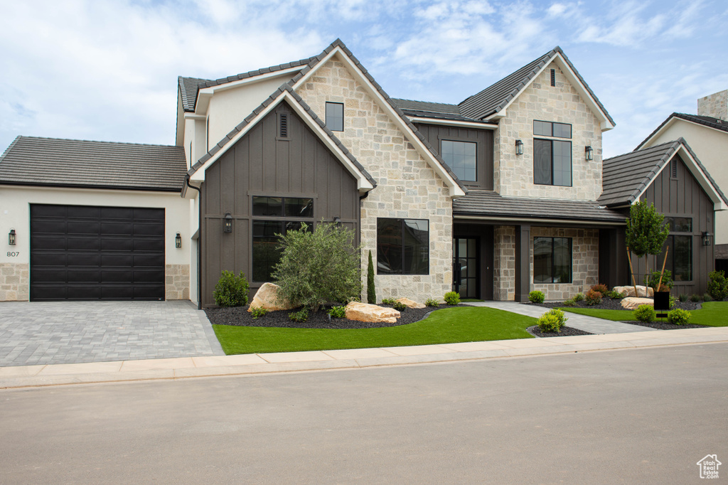 View of front of house with board and batten siding, stone siding, an attached garage, and driveway