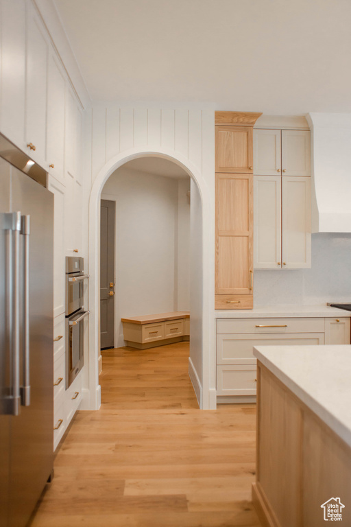 Kitchen featuring appliances with stainless steel finishes, arched walkways, light countertops, white cabinets, and light wood-type flooring