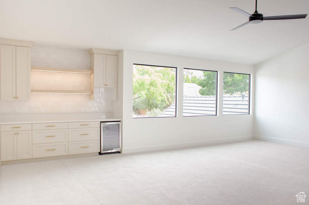 Interior space featuring wine cooler, light carpet, ceiling fan, and baseboards