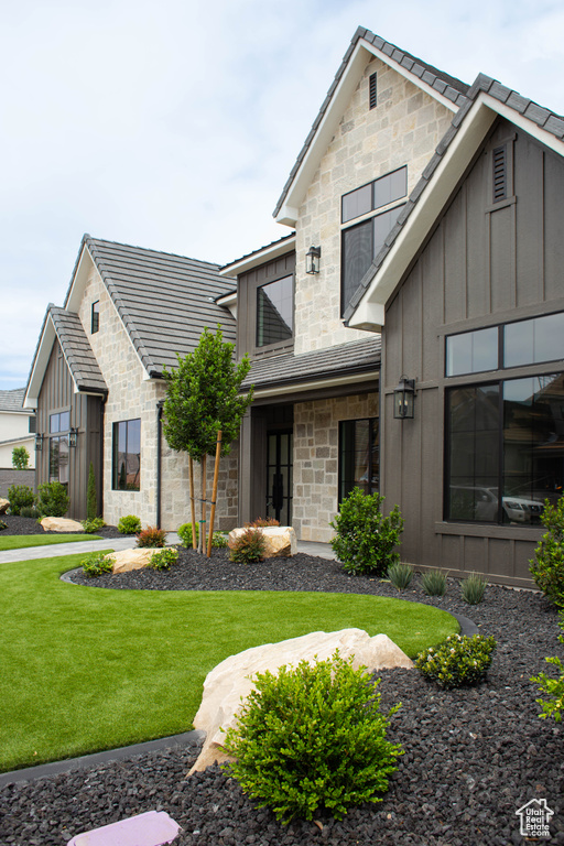 View of front of property featuring a front yard, a tiled roof, stone siding, and board and batten siding