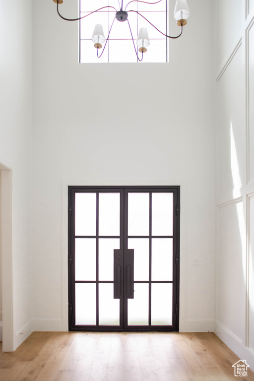 Interior space featuring baseboards, light wood-style floors, french doors, and a towering ceiling