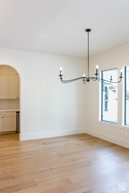 Unfurnished dining area with beverage cooler, a notable chandelier, light wood-type flooring, baseboards, and arched walkways