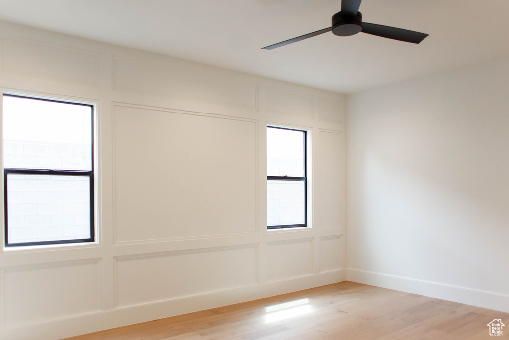 Empty room with light wood-type flooring, baseboards, a decorative wall, and ceiling fan