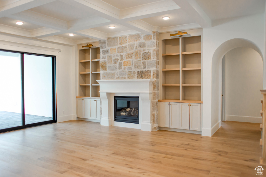 Unfurnished living room featuring coffered ceiling, light wood-type flooring, baseboards, beamed ceiling, and a large fireplace