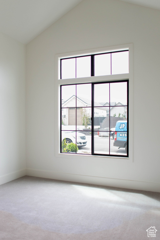 Spare room with vaulted ceiling, carpet floors, and baseboards
