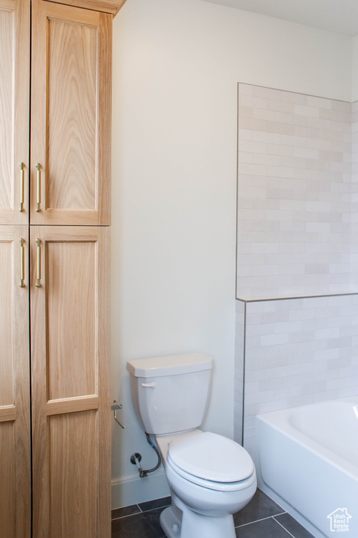 Full bathroom featuring toilet, baseboards, tile patterned floors, and a tub to relax in