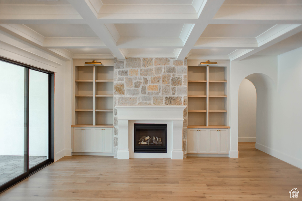 Unfurnished living room with light wood finished floors, beamed ceiling, arched walkways, and a large fireplace