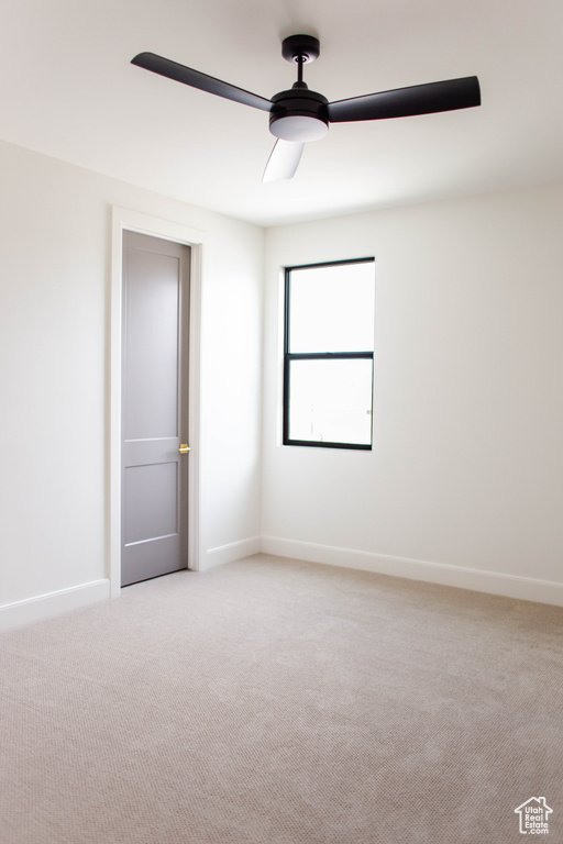 Empty room featuring light carpet, baseboards, and ceiling fan