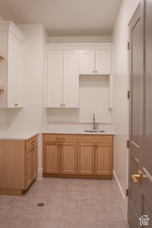 Kitchen with a sink, white cabinetry, light countertops, and baseboards