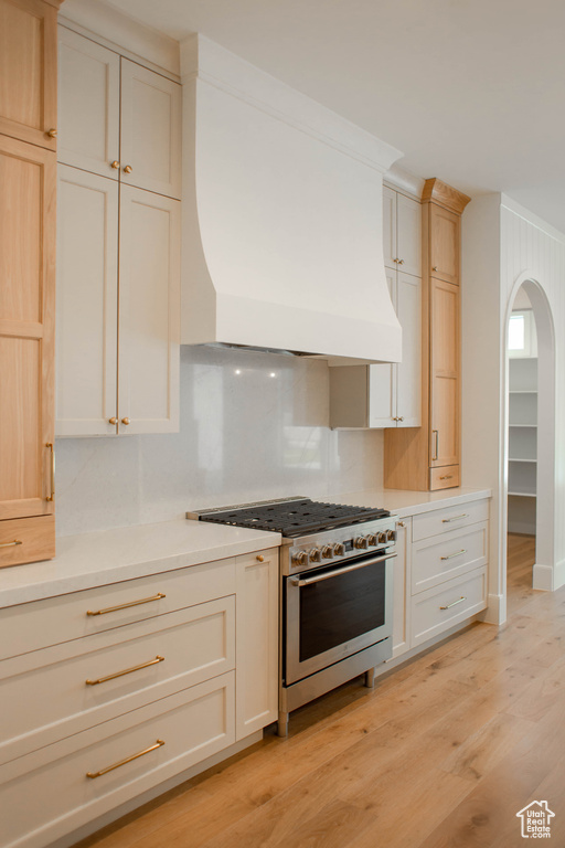 Kitchen featuring light wood-type flooring, high end stainless steel range oven, light countertops, decorative backsplash, and custom range hood