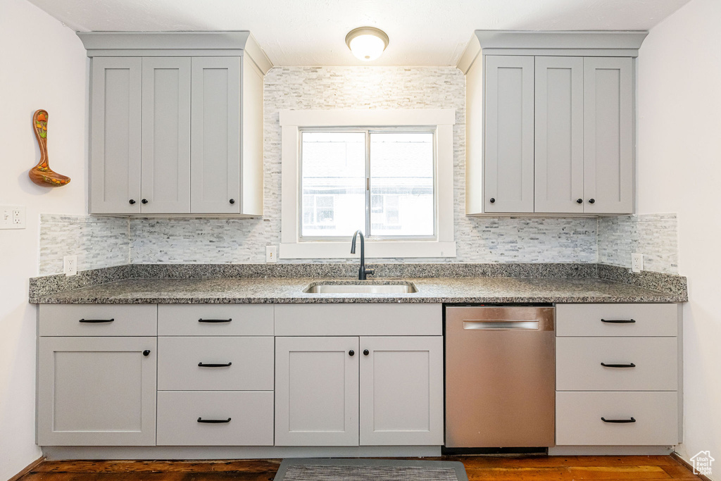 Kitchen featuring stainless steel dishwasher, a sink, decorative backsplash, and dark wood-style floors