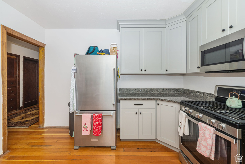 Kitchen with appliances with stainless steel finishes, light wood finished floors, and dark stone counters