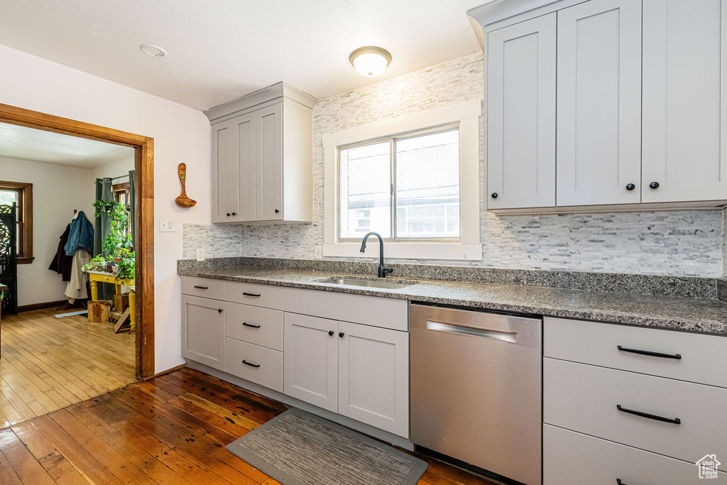 Kitchen featuring dishwasher, a sink, dark wood-style flooring, tasteful backsplash, and dark countertops