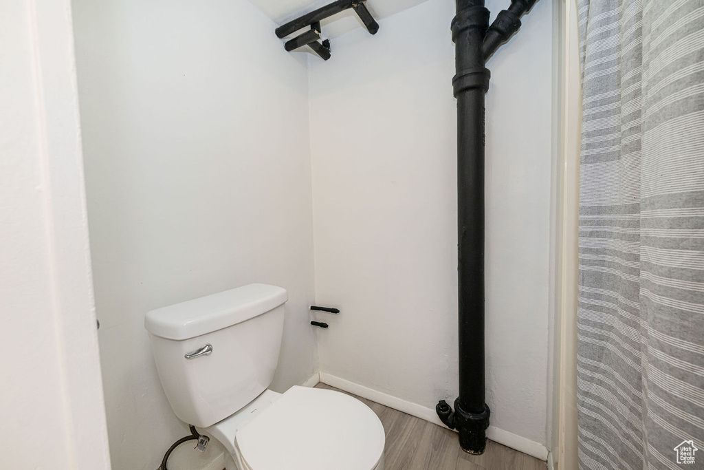 Full bathroom with wood finished floors, toilet, baseboards, and a shower with curtain