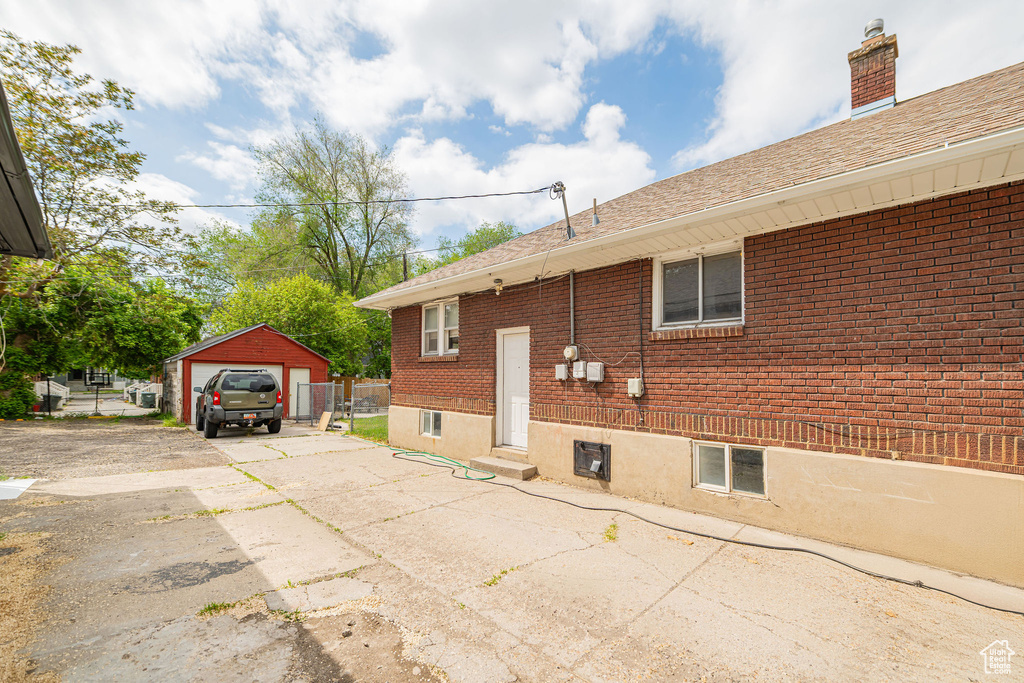 View of side of property featuring driveway, a detached garage, brick siding, and a shingled roof