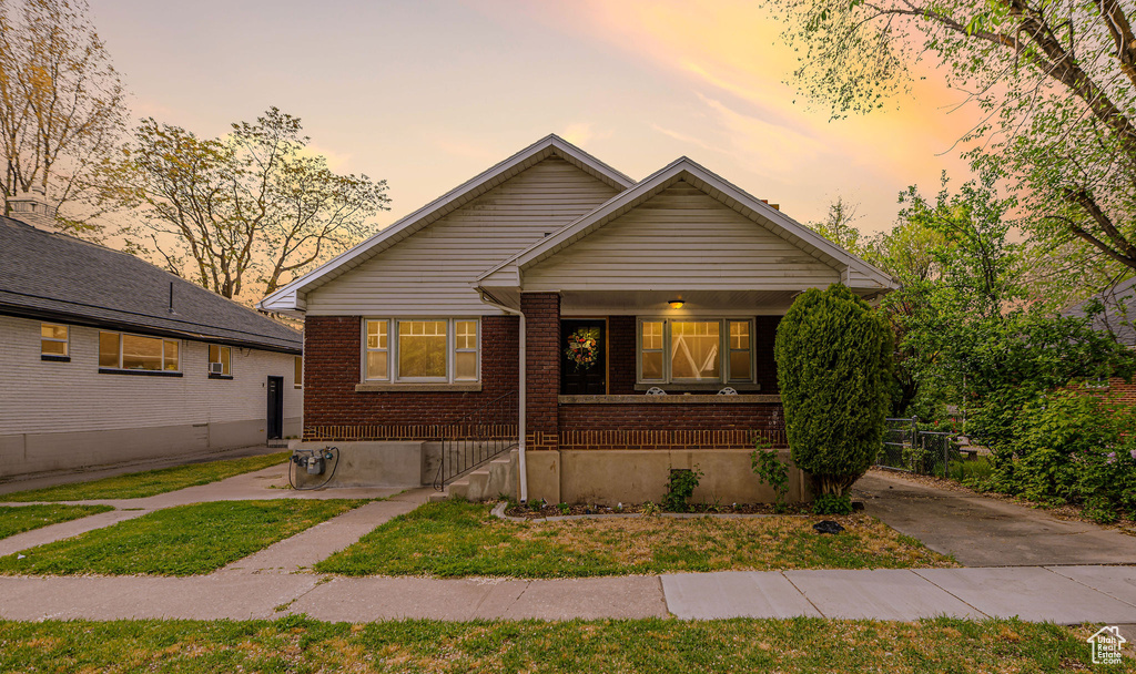 Bungalow-style house with brick siding, a porch, and a lawn