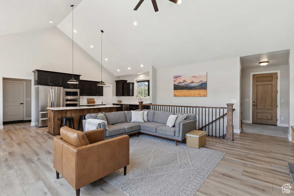 Living room with light wood-style flooring, high vaulted ceiling, baseboards, ceiling fan, and recessed lighting