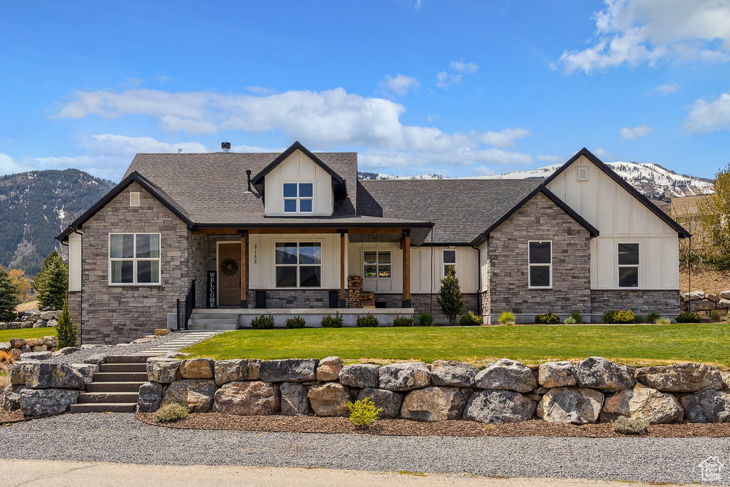 View of front of property with stone siding, a mountain view, board and batten siding, a front yard, and roof with shingles