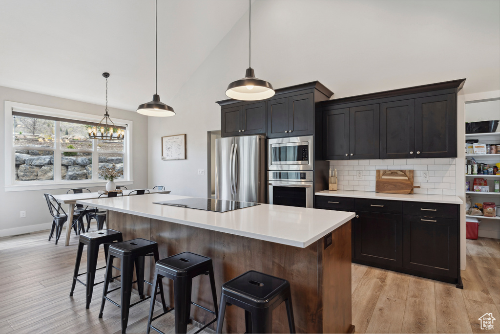 Kitchen featuring a notable chandelier, stainless steel appliances, a center island, a kitchen bar, and light countertops