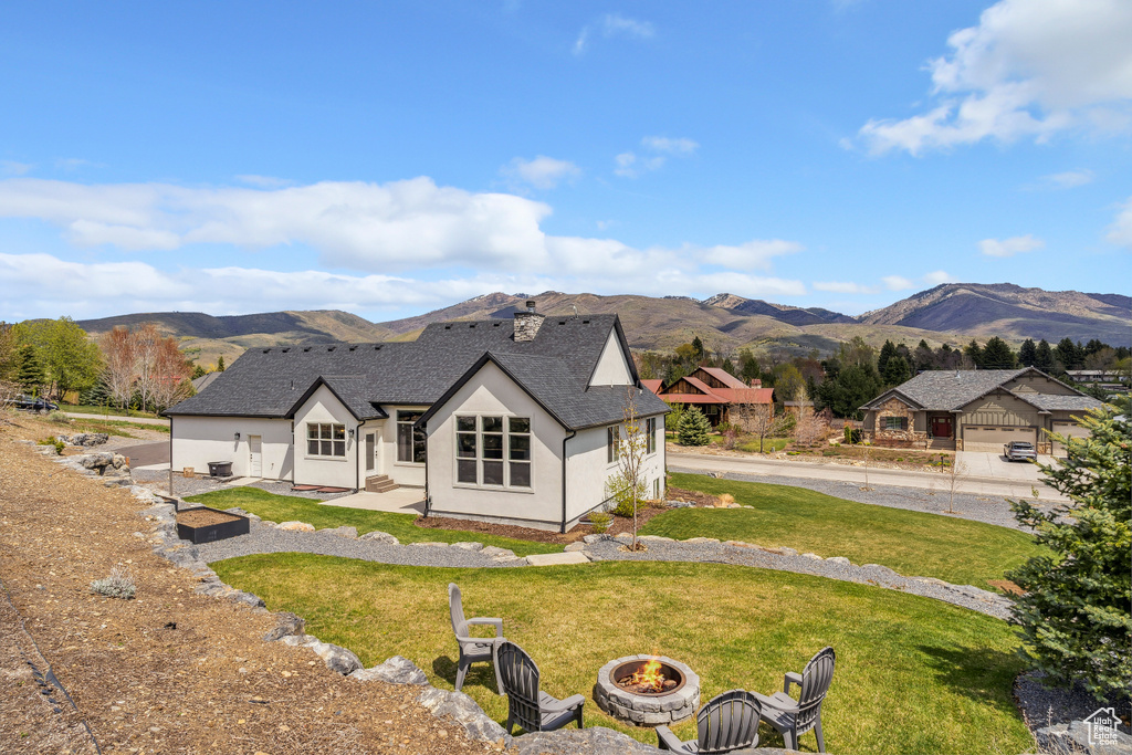 Back of house featuring a lawn, a mountain view, an outdoor fire pit, stucco siding, and a shingled roof