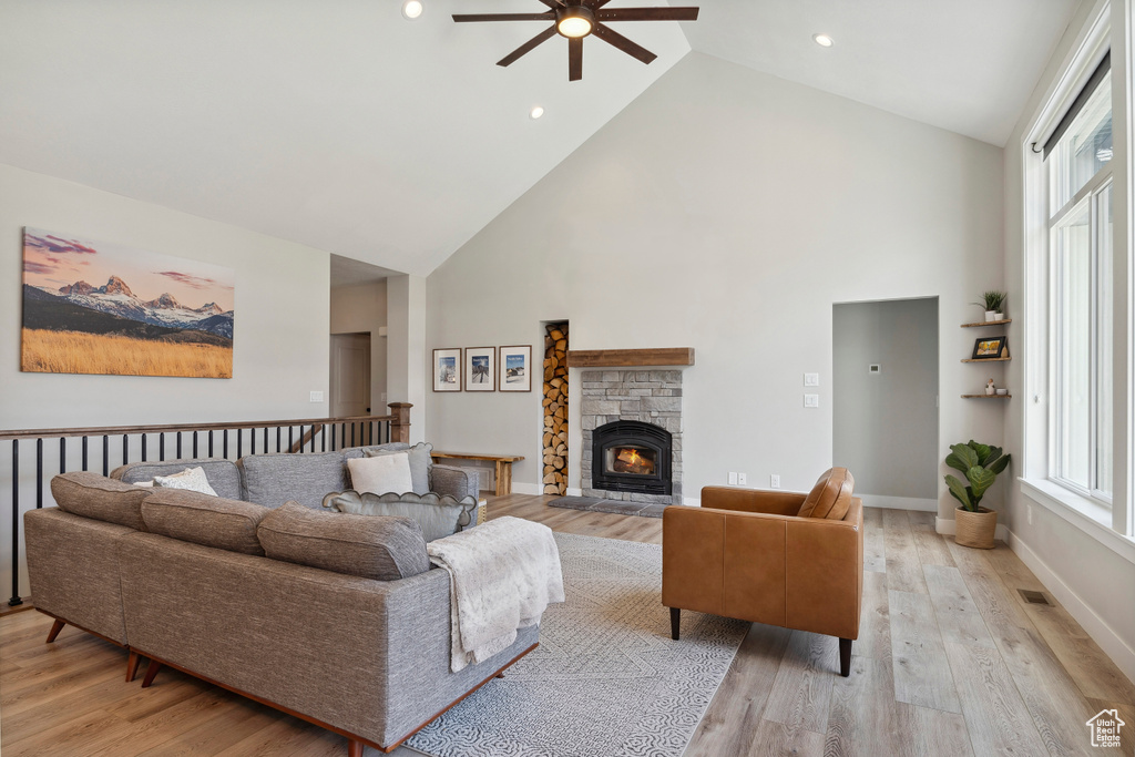 Living room featuring light wood-style flooring, high vaulted ceiling, a fireplace, visible vents, and ceiling fan