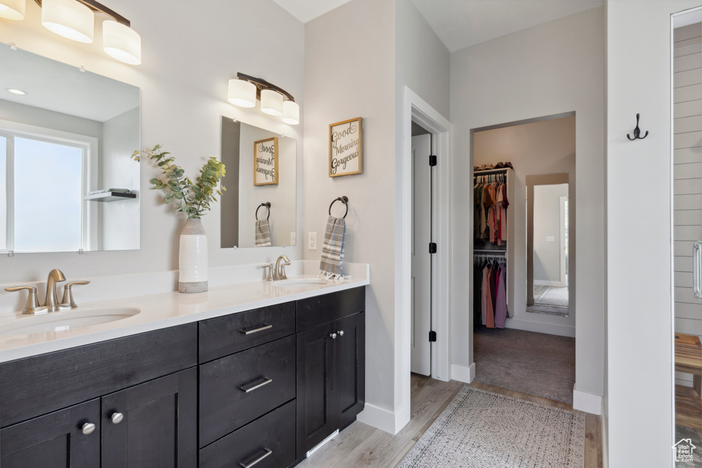 Bathroom featuring baseboards, a sink, double vanity, wood finished floors, and a spacious closet