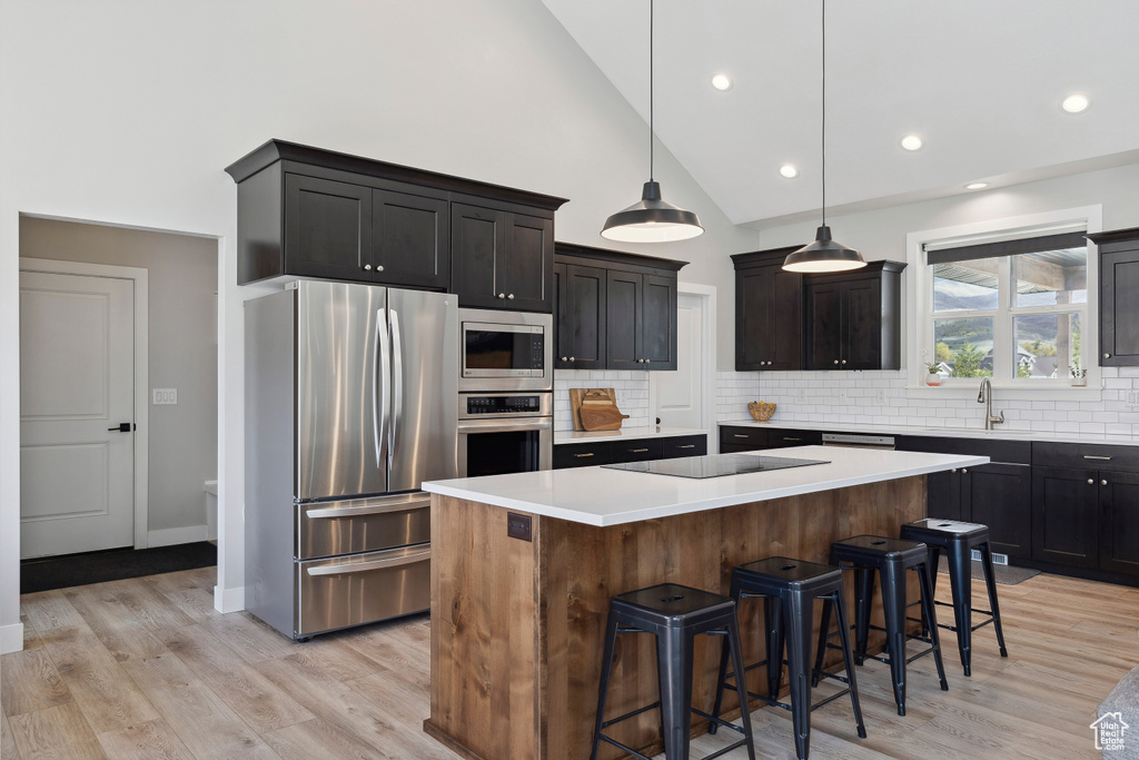 Kitchen with a center island, stainless steel appliances, a kitchen breakfast bar, light countertops, and tasteful backsplash