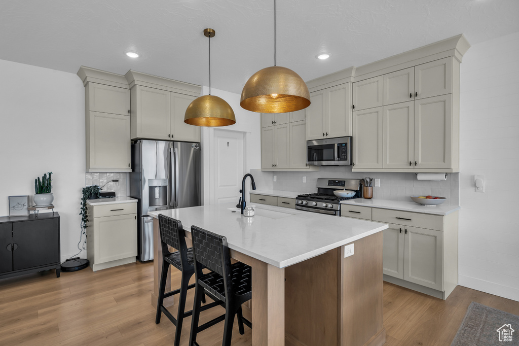 Kitchen featuring stainless steel appliances, a sink, light wood-style flooring, decorative backsplash, and a breakfast bar