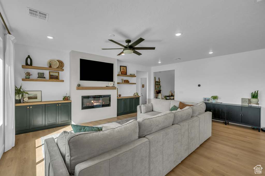 Living area with a ceiling fan, a glass covered fireplace, light wood-style floors, and recessed lighting