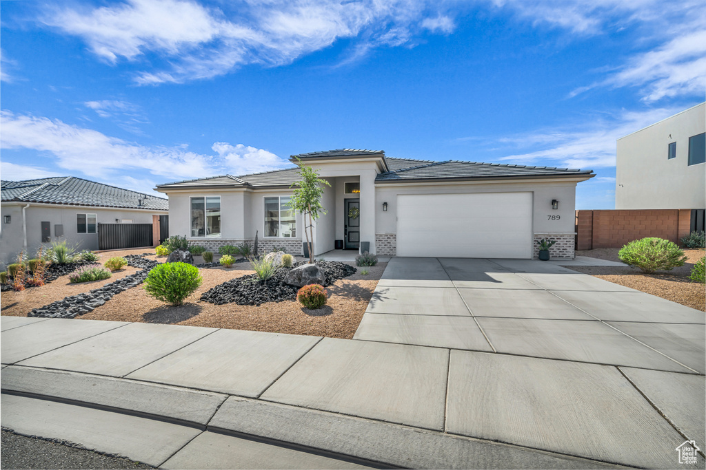 Prairie-style house with an attached garage, stucco siding, driveway, and a tiled roof